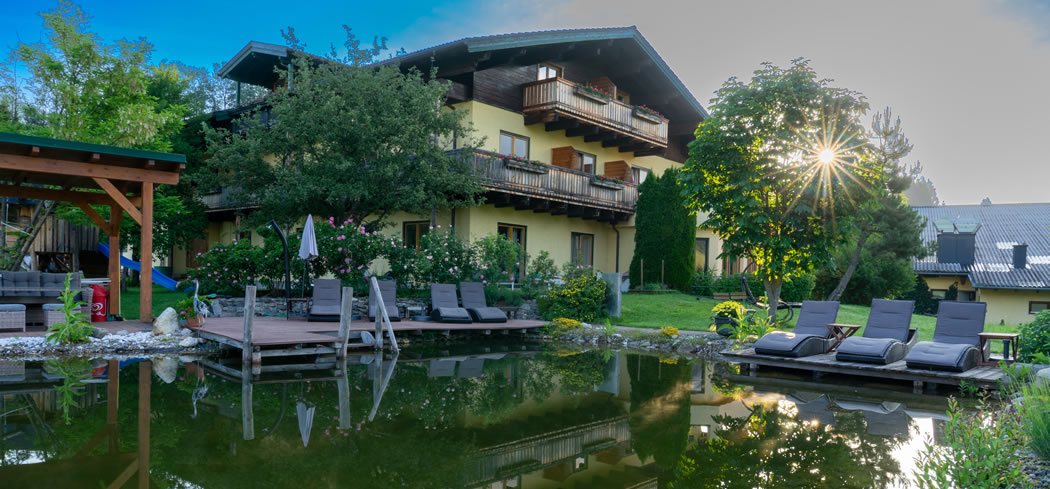 Die Sportpension Goldegg im Sommer mit Natur-Badeteich und Golfplatz vor der Haust&uuml;re